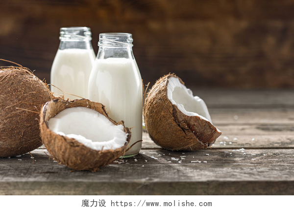 桌子上两瓶椰子奶和掰开的椰子放在木制桌子上的玻璃瓶中的椰子汁。 一种非乳制品的健康或发酵的饮料。 健康饮食概念